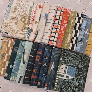 May include: A collection of folded fabric squares featuring various nautical and coastal patterns including boats, lobsters, crabs, shells, and seaside cottages in a color palette of navy, cream, olive green, light blue, and burnt orange.