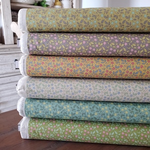 Może przedstawiać: Stos rolek materiału w różnych kolorach, każda ozdobiona delikatnym kwiatowym wzorem. Kolory obejmują oliwkową zieleń, zakurzony fiolet, złoty żółty, jasny beż, turkus i jasną zieleń. Materiał jest ciasno zwinięty, prezentując szczegółowe kwiatowe wzory.