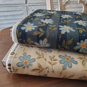 May include: Two fabric rolls with floral patterns. One roll features a navy blue background with vertical stripes and large blue flowers with orange centers. The other roll has a cream background with similar floral and leaf designs.