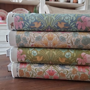 May include: Four fabric rolls with floral and bird designs. The top roll is blue with pink flowers and orange birds. The second roll is cream with orange and blue flowers. The third roll is green with orange birds and pink flowers. The bottom roll is cream with pink flowers.