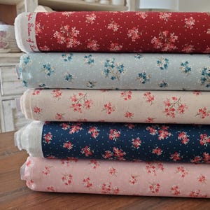 Pode incluir: Uma pilha de rolos de tecido em várias cores, incluindo vermelho, azul claro, bege, azul marinho e rosa. Cada rolo apresenta um padrão floral com pequenos pontos brancos. O tecido é provavelmente algodão, adequado para projetos de costura.