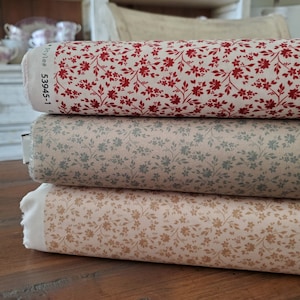 Puede incluir: Tres rollos de tela floral en rojo, gris verdoso y beige. Cada rollo presenta un patrón repetido de pequeñas flores y hojas. La tela está bien enrollada, con los bordes de la tela visibles, mostrando el número de estilo.