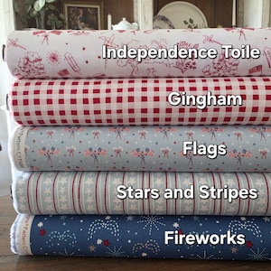 May include: A stack of fabric rolls with patriotic patterns. The top roll is white with red Independence Toile designs. Below it is red gingham, followed by a light blue Flags print, then Stars and Stripes, and finally, a blue Fireworks pattern.