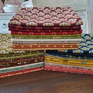 May include: Stacks of patterned fabric in various colors, including red, green, and blue. The fabric features floral and geometric designs. The stacks are neatly arranged on a wooden surface, showcasing a variety of patterns and colors.