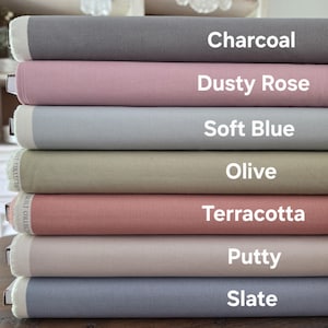 Puede incluir: Una pila de rollos de tela en varios colores, incluyendo carbón, rosa empolvado, azul suave, oliva, terracota, masilla y pizarra. Cada rollo está etiquetado con su nombre de color en texto blanco. La tela tiene una apariencia texturizada.