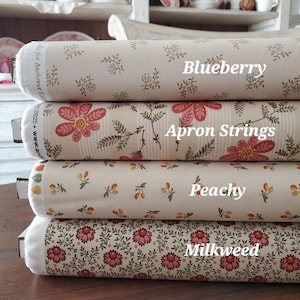 May include: Four rolls of fabric stacked on top of each other. Each roll has a different floral pattern and color scheme. The fabric names are Blueberry, Apron Strings, Peachy, and Milkweed. The fabric is beige, cream, and brown.