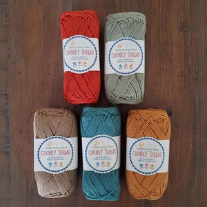 May include: Five skeins of colorful chunky cotton yarn in shades of red, green, tan, teal, and orange. Each skein has a label that reads "100% Cotton Yarn CHUNKY THREAD" with a bee and flower design.
