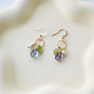 May include: A pair of gold earrings with a purple and blue glass bead, a small white pearl, and a green leaf charm on each earring.