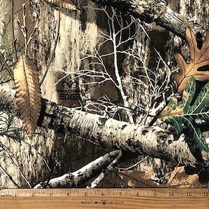 May include: A close-up of a brown, green, and white camouflage fabric with the text "RealTree EDGE" printed on it. A ruler is visible at the bottom of the image.