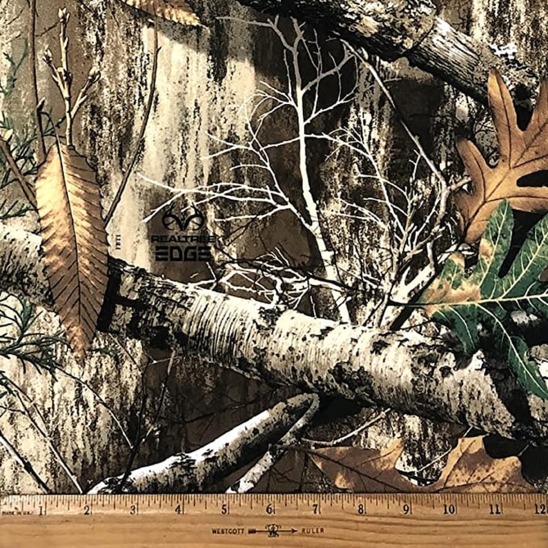 May include: A close-up of a brown, green, and white camouflage fabric with the text "RealTree EDGE" printed on it. A ruler is visible at the bottom of the image.