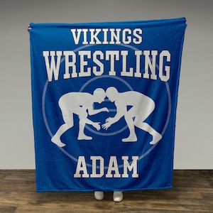 May include: Blue fleece blanket with the text "VIKINGS WRESTLING ADAM" in white. The blanket features a white silhouette of two wrestlers in a circle.