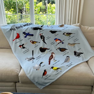 May include: A blue fleece blanket with a white background and colorful illustrations of different birds. The text "My Bird Watch" is at the top of the blanket.