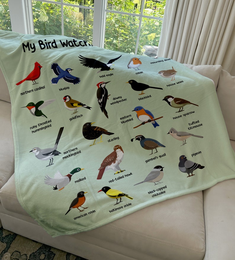 May include: A green fleece blanket with a colorful illustration of various birds. The blanket features the text "My Bird Watch" at the top and names each bird species below its image.