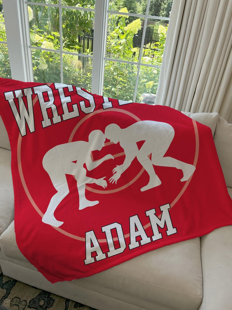 May include: Red fleece blanket with a white wrestling silhouette and the name "ADAM" in white text.