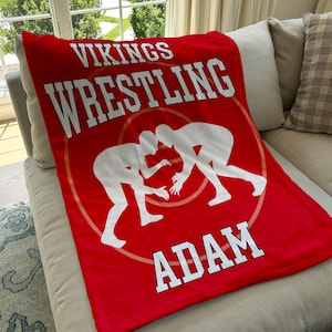 May include: Red fleece blanket with white text that reads "Vikings Wrestling Adam" and a silhouette of two wrestlers in the center.