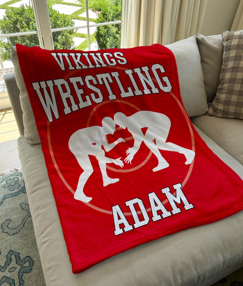 May include: Red fleece blanket with white text that reads "Vikings Wrestling Adam" and a silhouette of two wrestlers in the center.