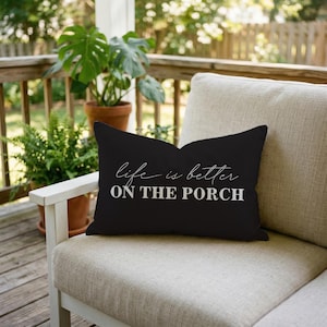 May include: A white ceramic mug with a black handle and the text "But First, Coffee" in a bold, black font. The mug is set against a blurred background, suggesting a cozy setting. The mug appears to be approximately 4 inches tall.