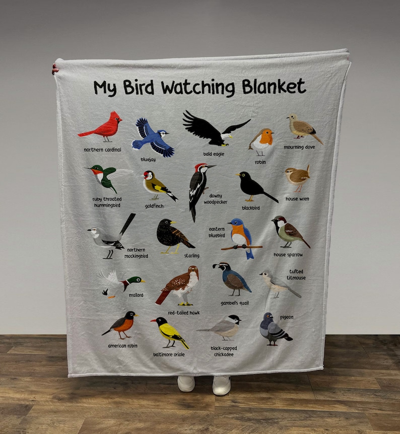 May include: A white fleece blanket with a colorful illustration of different bird species. The blanket features the text "My Bird Watching Blanket" at the top. Each bird is labeled with its name.