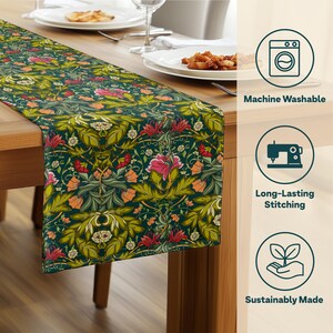 May include: A dark green table runner with a floral pattern featuring pink, orange, and yellow flowers and green leaves. The runner is placed on a wooden table, with plates and silverware visible.
