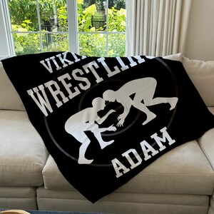 May include: Black fleece blanket with white text that reads "Viking Wrestling Adam" and a graphic of two wrestlers in silhouette.