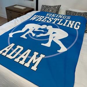 May include: Blue wrestling blanket with white silhouettes of wrestlers and the text "Vikings Wrestling Adam".