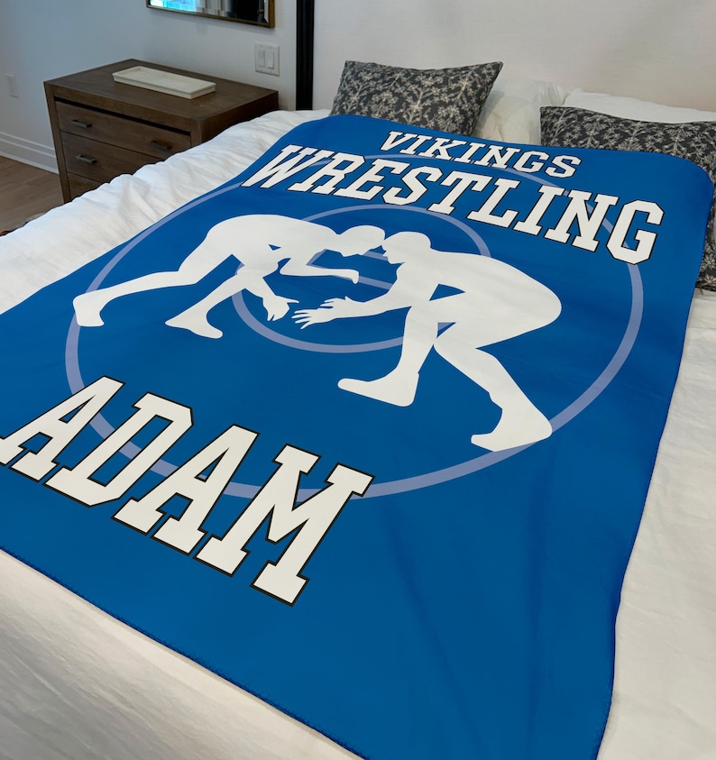 May include: Blue wrestling blanket with white silhouettes of wrestlers and the text "Vikings Wrestling Adam".