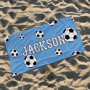 May include: A light blue beach towel with a soccer ball pattern and the name "JACKSON" printed in white.