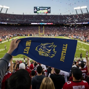 May include: A navy blue flag with the words "LEANS" and "FOOTBALL" in gold lettering. The flag features a gold lion graphic. The flag is being held up in a crowded stadium during a football game.