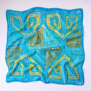 May include: A square, silk scarf with a vibrant geometric design. The scarf features a turquoise background with yellow and teal accents. The pattern includes spiral and angular shapes, creating a bold and artistic look. The scarf is signed in the bottom right corner.