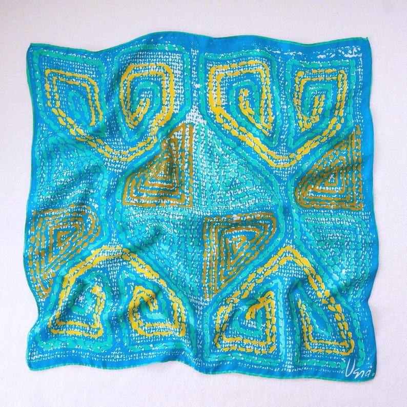 May include: A square, silk scarf with a vibrant geometric design. The scarf features a turquoise background with yellow and teal accents. The pattern includes spiral and angular shapes, creating a bold and artistic look. The scarf is signed in the bottom right corner.