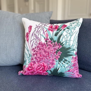 May include: A white cushion with a floral print featuring pink and green flowers. The cushion is on a blue sofa.