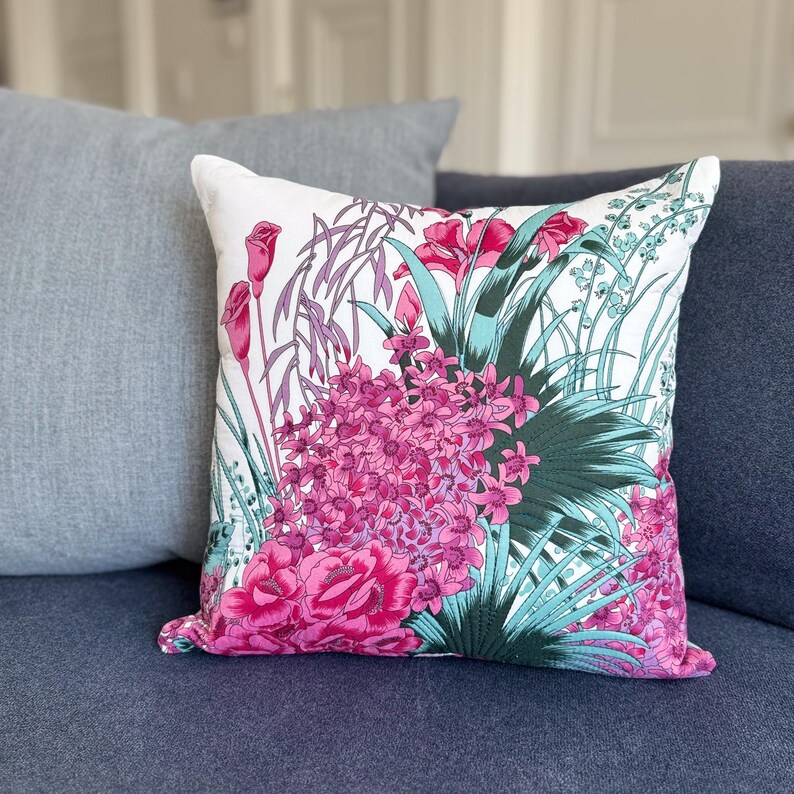 May include: A white cushion with a floral print featuring pink and green flowers. The cushion is on a blue sofa.