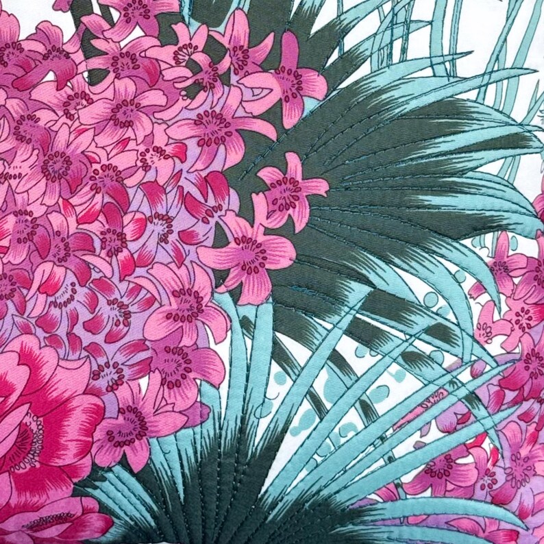 May include: A pink and white floral fabric with a green and blue leaf pattern. The fabric has a quilted texture.