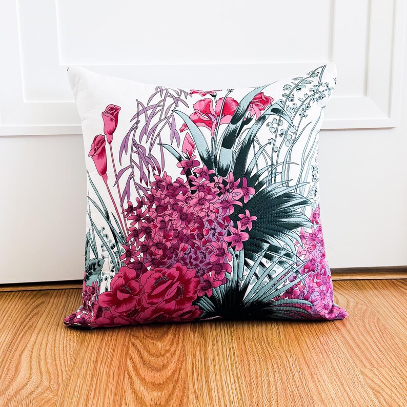 May include: A white cushion with a floral print featuring pink and green flowers. The cushion is on a wooden floor.