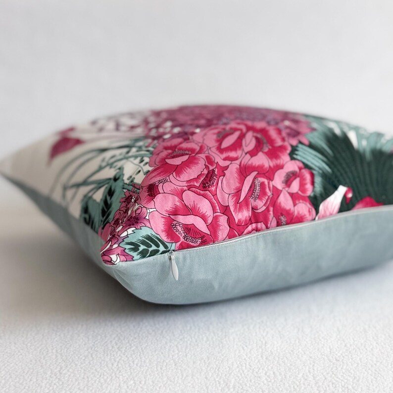 May include: A decorative cushion with a floral print featuring pink and green flowers on a white background. The cushion has a light blue back and a zipper closure.