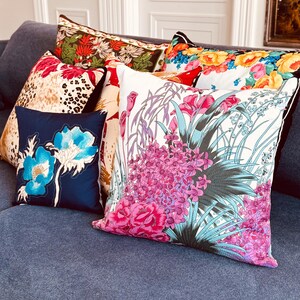 May include: A collection of decorative throw pillows with floral patterns. The pillows are arranged on a blue sofa. The pillows feature a variety of colours, including pink, blue, green, and yellow.