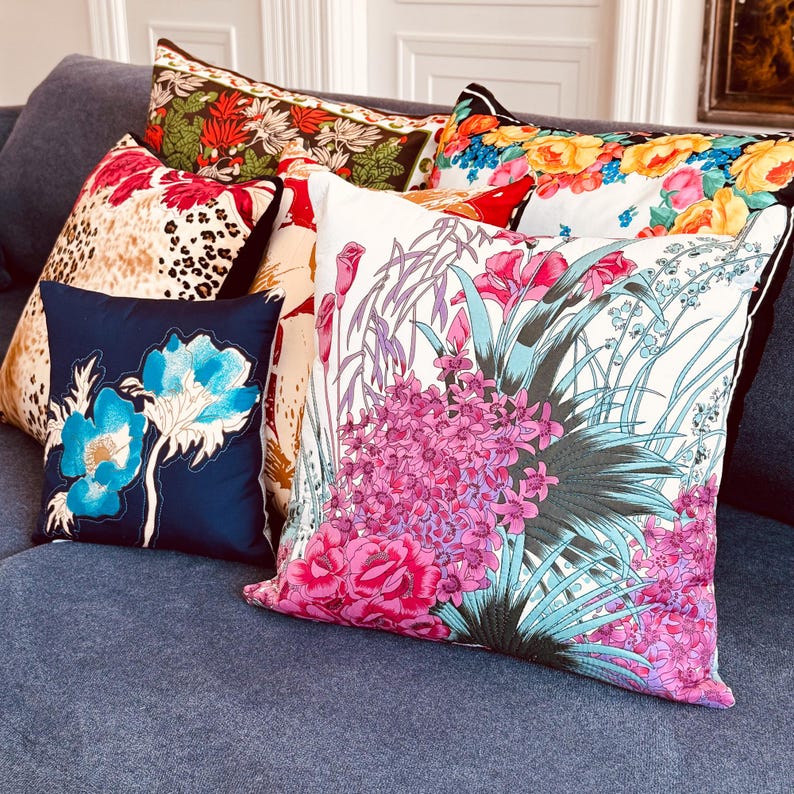 May include: A collection of decorative throw pillows with floral patterns. The pillows are arranged on a blue sofa. The pillows feature a variety of colours, including pink, blue, green, and yellow.
