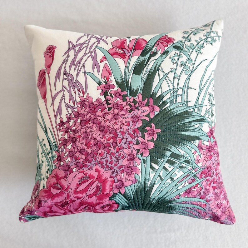 May include: A white cushion with a floral print featuring pink and green flowers. The cushion is made of a soft, comfortable fabric and has a subtle sheen.