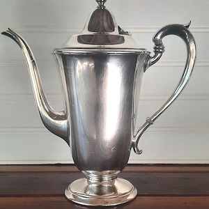 May include: A silver teapot with a lid and a curved handle. The teapot has a classic design and a polished finish.