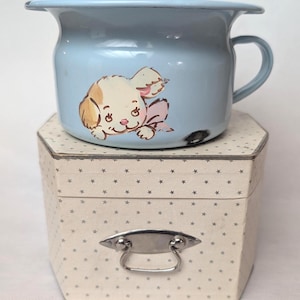 May include: A light blue enamel potty with a handle and a painted puppy design. The potty sits atop a hexagonal box with a star pattern and a silver handle.
