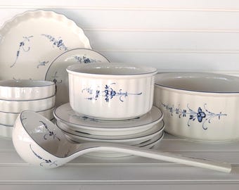 May include: A collection of white ceramic tableware with blue floral designs. The set includes plates, bowls, a serving dish, and a ladle. The pieces have a scalloped edge and a blue trim.
