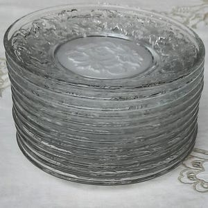 May include: A stack of clear glass plates with a raised floral design. The plates are stacked on top of each other, creating a tower of plates.