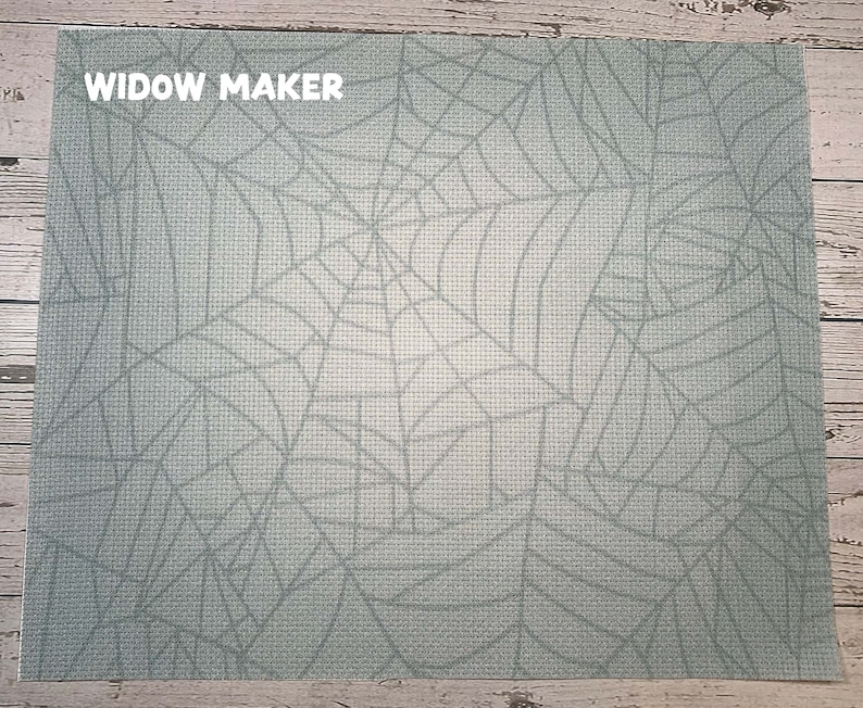 May include: A rectangular placemat with a light blue spiderweb design. The text "WIDOW MAKER" is printed in white in the upper left corner. The placemat has a textured appearance.