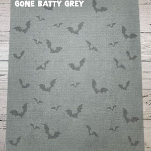 May include: A gray fabric with a repeating pattern of dark gray bat silhouettes. The text "GONE BATTY GREY" is printed in white at the top. The fabric has a textured appearance, suitable for Halloween-themed crafts.