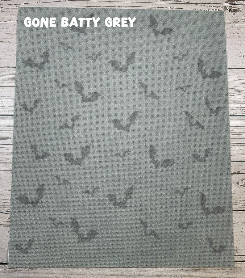 May include: A gray fabric with a repeating pattern of dark gray bat silhouettes. The text "GONE BATTY GREY" is printed in white at the top. The fabric has a textured appearance, suitable for Halloween-themed crafts.