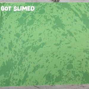 May include: A rectangular green mat with a textured surface and a splattered pattern in varying shades of green. The white text "I GOT SLIMED" is printed at the top left corner of the mat. The mat is likely used for crafting or play.