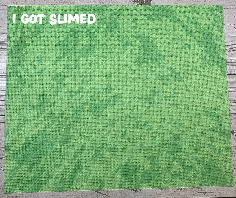 May include: A rectangular green mat with a textured surface and a splattered pattern in varying shades of green. The white text "I GOT SLIMED" is printed at the top left corner of the mat. The mat is likely used for crafting or play.