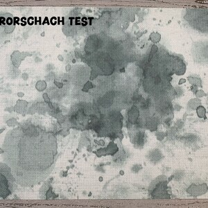 May include: A rectangular textile with a white background and a pattern of gray watercolor-like blotches and splatters. The text "RORSCHACH TEST" is printed in black at the top. The textile has a cross-stitch appearance.