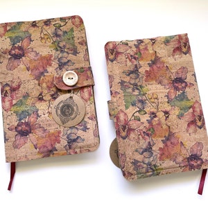 May include: Two cork notebooks with floral patterns and red ribbon closures. The notebooks have a button closure and a small tag with a logo.