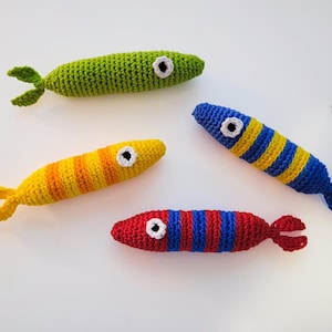 May include: Four crocheted fish toys in different colors. The fish are green, yellow, red, and blue with white eyes.